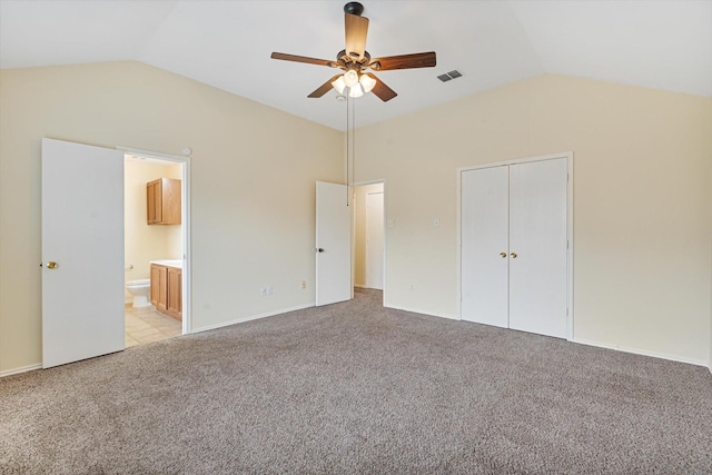 unfurnished bedroom featuring a closet, ensuite bathroom, vaulted ceiling, and light carpet