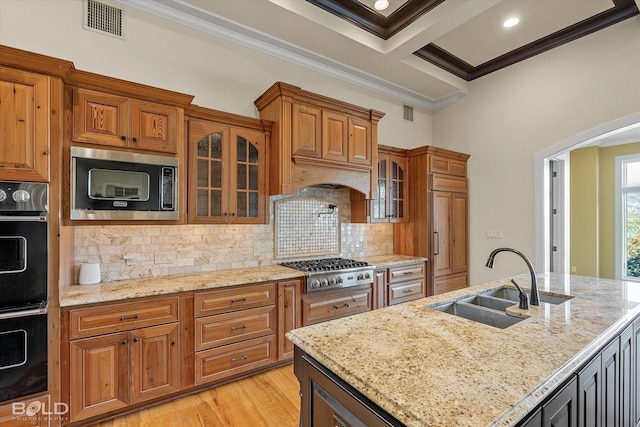 kitchen featuring sink, built in appliances, ornamental molding, light stone countertops, and a center island with sink