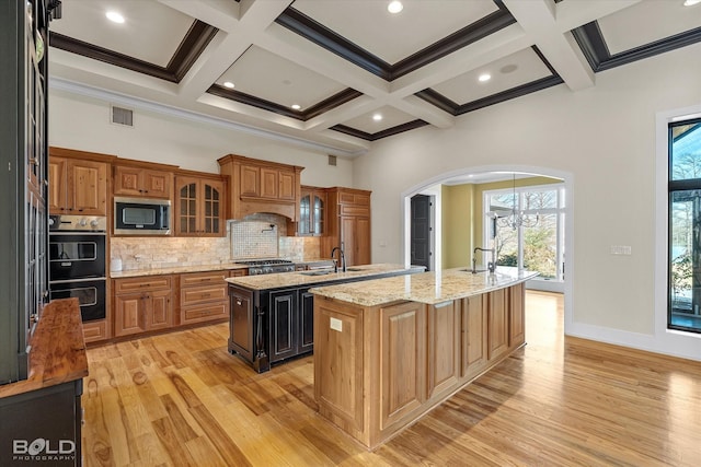 kitchen featuring built in microwave, an island with sink, decorative backsplash, light hardwood / wood-style floors, and light stone counters