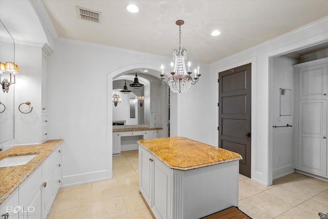 kitchen with sink, white cabinetry, a center island, light stone counters, and ornamental molding