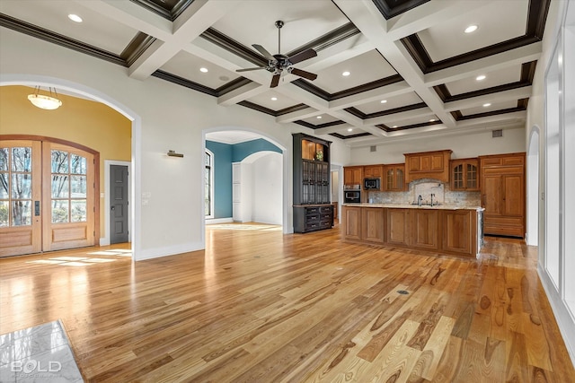 kitchen with tasteful backsplash, beamed ceiling, a towering ceiling, wall oven, and light hardwood / wood-style floors