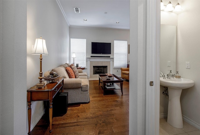 living room with sink, crown molding, a tile fireplace, and dark hardwood / wood-style floors