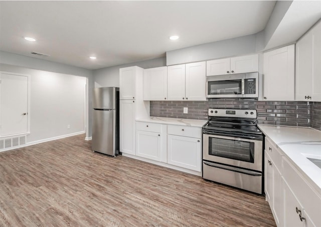 kitchen with appliances with stainless steel finishes, tasteful backsplash, white cabinetry, light stone counters, and light wood-type flooring