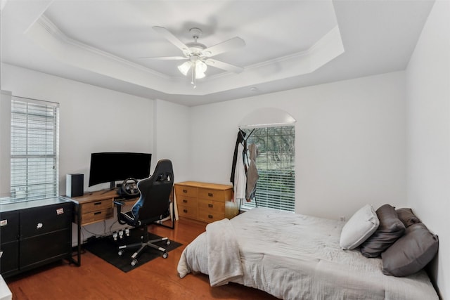 bedroom with hardwood / wood-style floors, crown molding, a raised ceiling, and ceiling fan