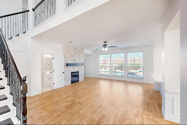 unfurnished living room with ceiling fan, a stone fireplace, light hardwood / wood-style floors, and a high ceiling