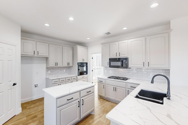 kitchen with sink, light stone countertops, black appliances, white cabinets, and light wood-type flooring