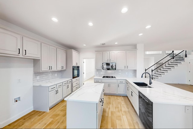 kitchen featuring sink, black appliances, kitchen peninsula, light stone countertops, and white cabinets