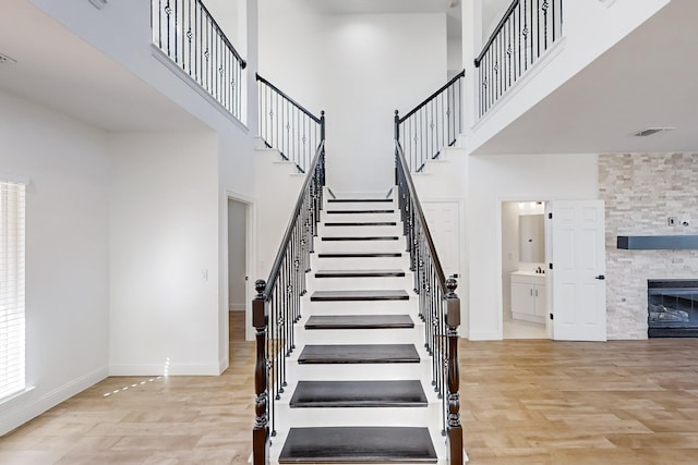 stairs with a stone fireplace, a towering ceiling, and hardwood / wood-style floors