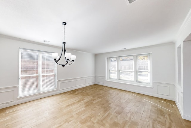 unfurnished dining area featuring ornamental molding, an inviting chandelier, and light wood-type flooring