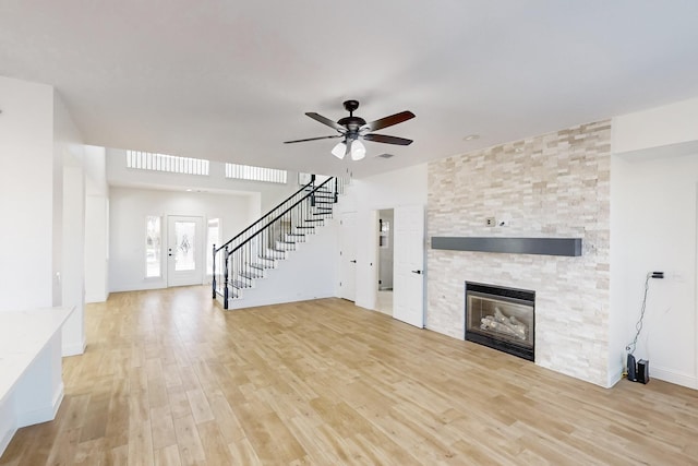 unfurnished living room featuring a stone fireplace, light hardwood / wood-style flooring, french doors, and ceiling fan