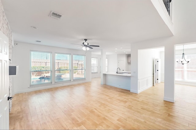 unfurnished living room with sink, ceiling fan with notable chandelier, and light hardwood / wood-style flooring