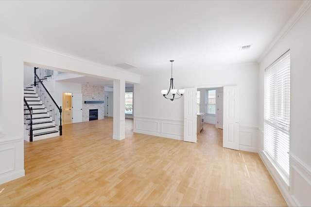 unfurnished living room with ornamental molding, a fireplace, light hardwood / wood-style flooring, and a notable chandelier