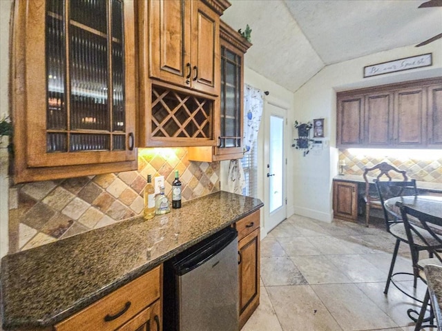 kitchen with tasteful backsplash, stainless steel dishwasher, dark stone counters, and lofted ceiling