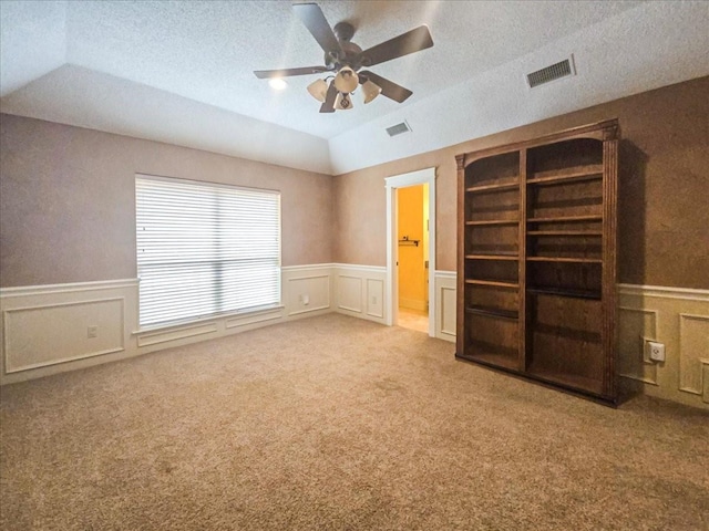 empty room with built in shelves, vaulted ceiling, a textured ceiling, ceiling fan, and carpet