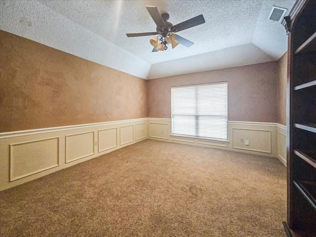 empty room featuring ceiling fan, lofted ceiling, carpet flooring, and a textured ceiling