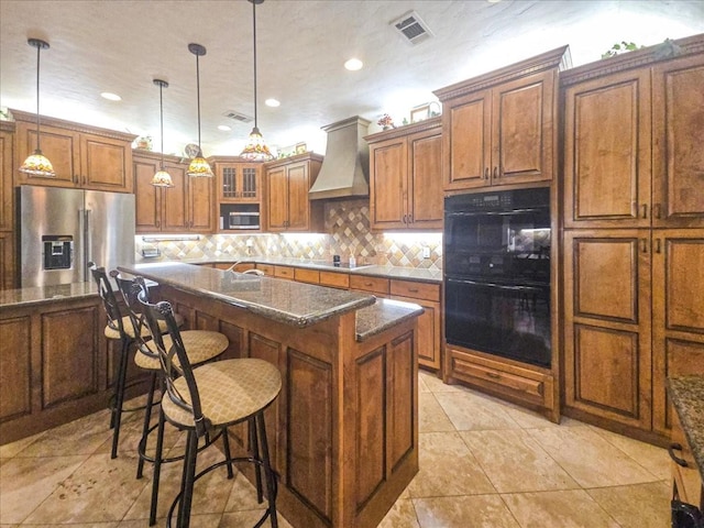 kitchen with custom exhaust hood, hanging light fixtures, a kitchen breakfast bar, a kitchen island with sink, and black appliances