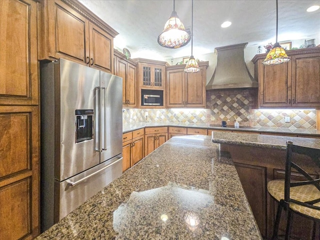 kitchen featuring pendant lighting, black electric stovetop, high quality fridge, custom range hood, and dark stone counters