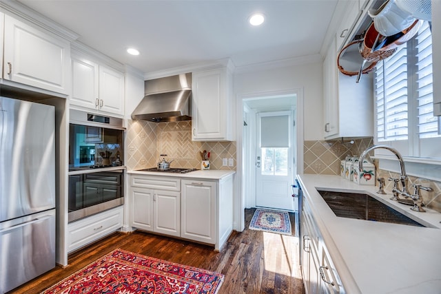 kitchen with wall chimney range hood, sink, appliances with stainless steel finishes, dark hardwood / wood-style floors, and white cabinets