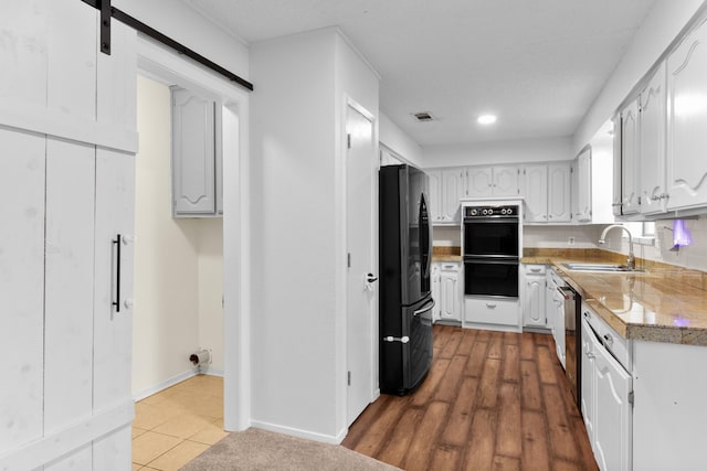 kitchen featuring white cabinets, a barn door, sink, and black appliances