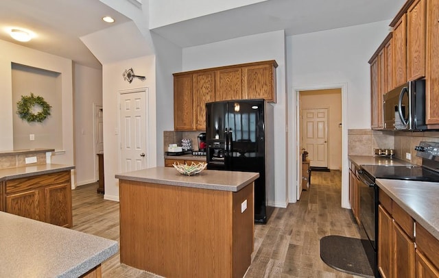 kitchen featuring decorative backsplash, black appliances, a center island, and light wood-type flooring