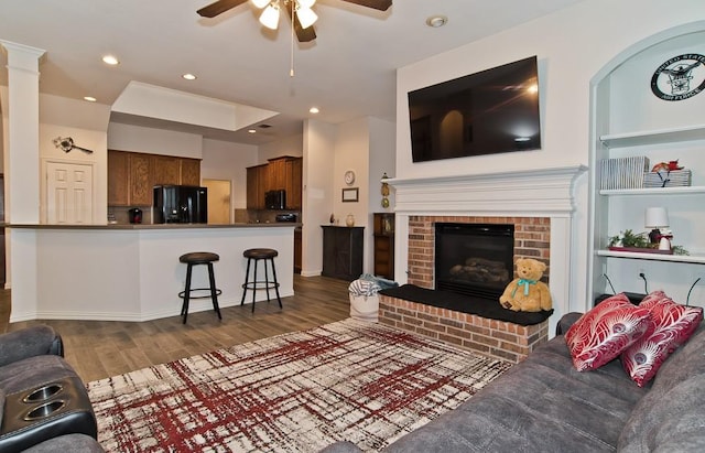 living room featuring a brick fireplace, dark wood-type flooring, and ceiling fan