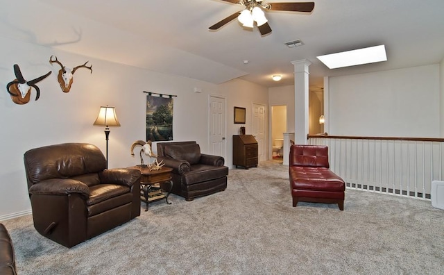 carpeted living room featuring decorative columns, ceiling fan, and a skylight