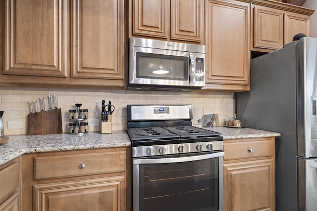 kitchen featuring stainless steel appliances, light stone counters, and decorative backsplash