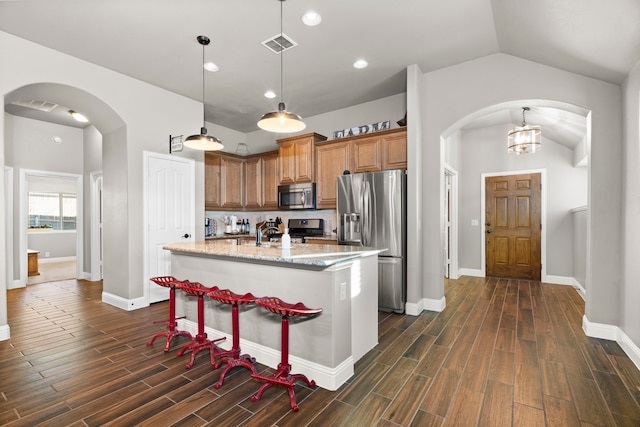 kitchen with lofted ceiling, light stone counters, an island with sink, pendant lighting, and stainless steel appliances