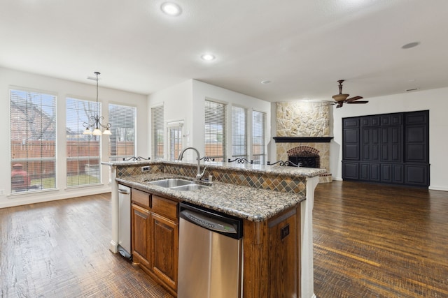 kitchen with pendant lighting, a fireplace, sink, a kitchen island with sink, and stainless steel dishwasher