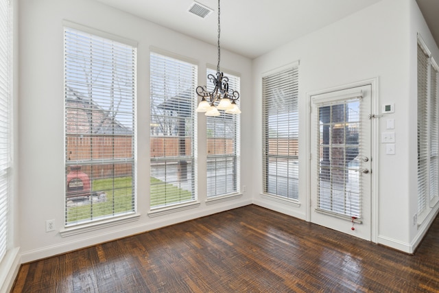 unfurnished dining area with plenty of natural light, dark wood-type flooring, and a notable chandelier