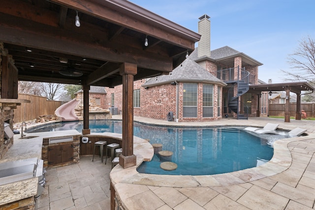 view of swimming pool featuring a water slide, exterior kitchen, a patio, and an outdoor wet bar