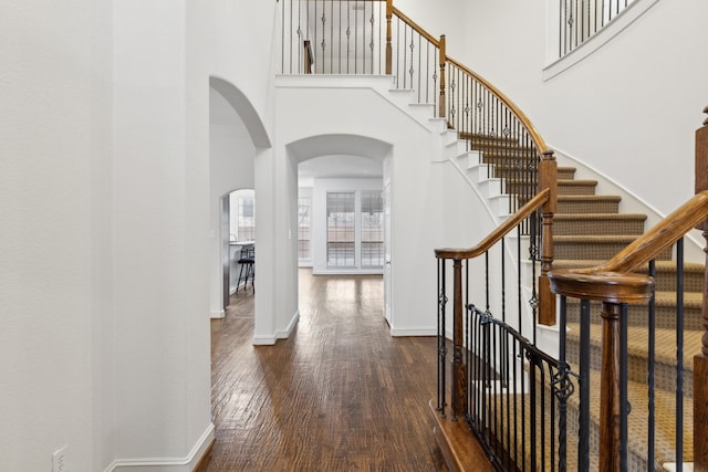 entryway with dark wood-type flooring and a towering ceiling