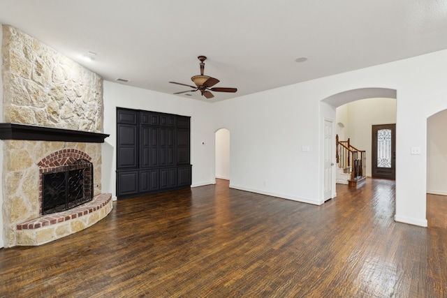 unfurnished living room with a stone fireplace, dark hardwood / wood-style floors, and ceiling fan