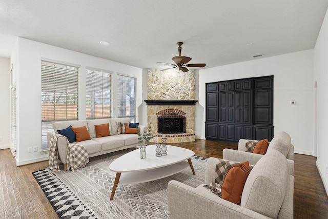 living room featuring dark hardwood / wood-style floors, ceiling fan, and a stone fireplace