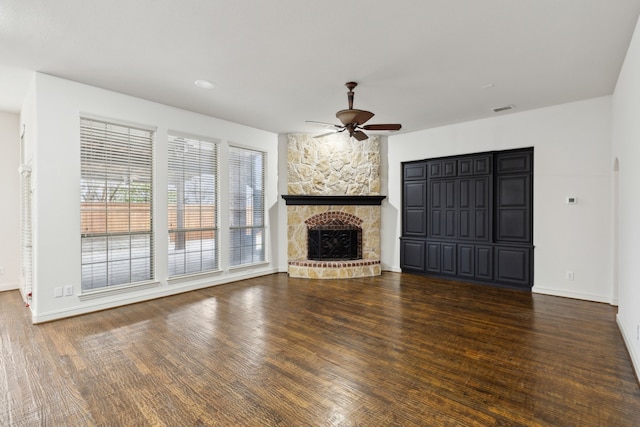 unfurnished living room featuring dark hardwood / wood-style floors, ceiling fan, and a stone fireplace