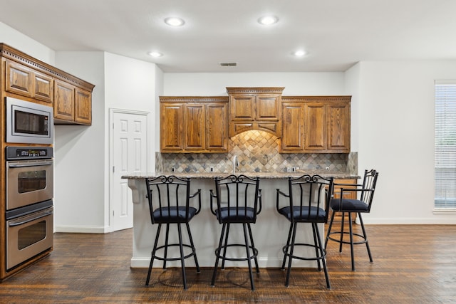 kitchen featuring stainless steel appliances, a breakfast bar, backsplash, and light stone counters