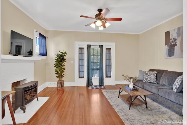 living room with hardwood / wood-style flooring, ceiling fan, crown molding, and a wood stove