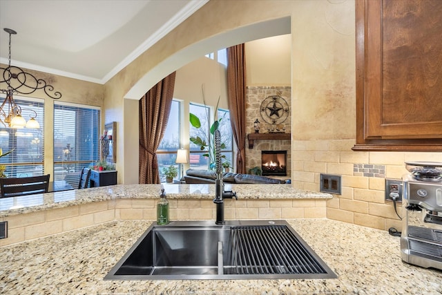 kitchen with light stone counters, hanging light fixtures, ornamental molding, a fireplace, and backsplash