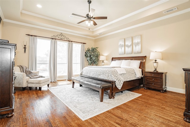 bedroom with a raised ceiling, ornamental molding, hardwood / wood-style flooring, and ceiling fan