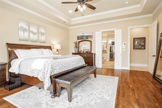 bedroom featuring a raised ceiling, ornamental molding, hardwood / wood-style flooring, and ceiling fan