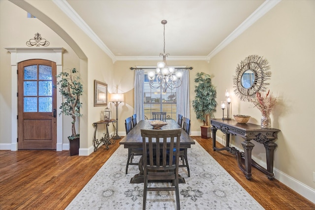 dining space with dark wood-type flooring, ornamental molding, and a chandelier