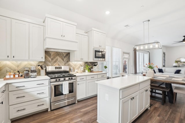 kitchen with appliances with stainless steel finishes, white cabinetry, tasteful backsplash, decorative light fixtures, and custom exhaust hood