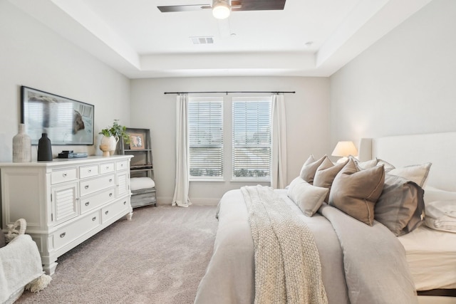 bedroom featuring light carpet, a tray ceiling, and ceiling fan