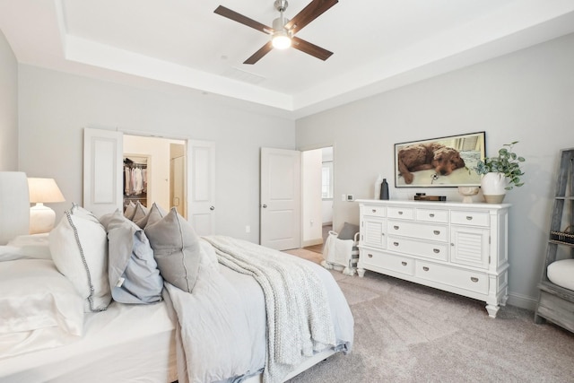 carpeted bedroom with a spacious closet, ceiling fan, and a tray ceiling