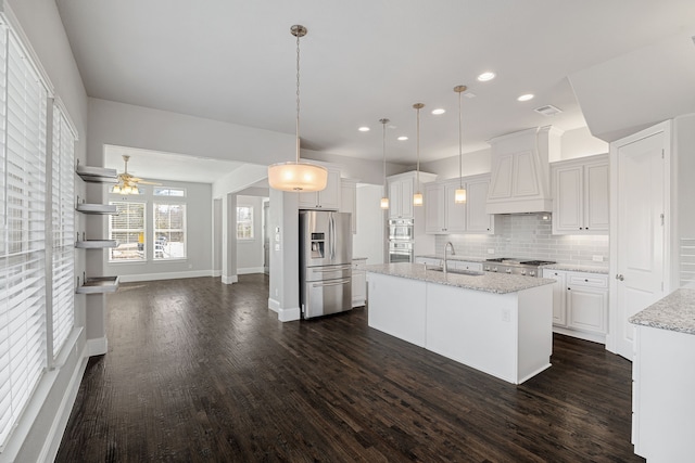 kitchen with stainless steel appliances, custom range hood, a center island with sink, and white cabinets