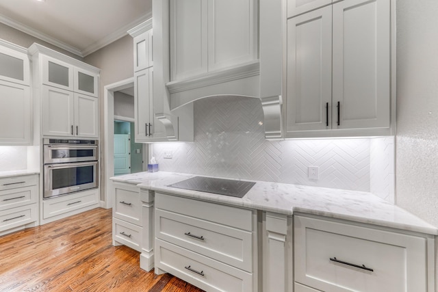 kitchen with white cabinets, ornamental molding, black electric stovetop, stainless steel double oven, and light hardwood / wood-style flooring