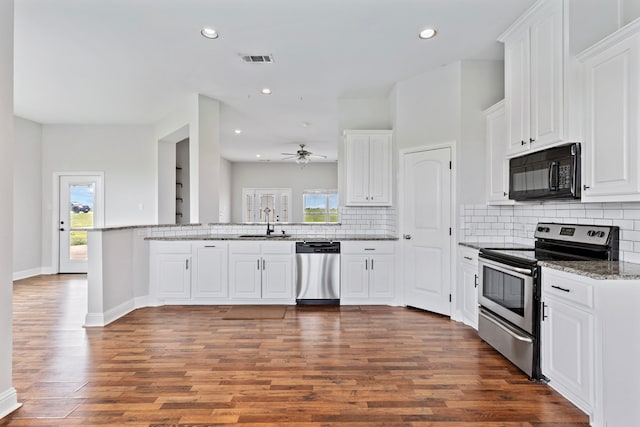 kitchen with appliances with stainless steel finishes, white cabinetry, sink, hardwood / wood-style flooring, and kitchen peninsula