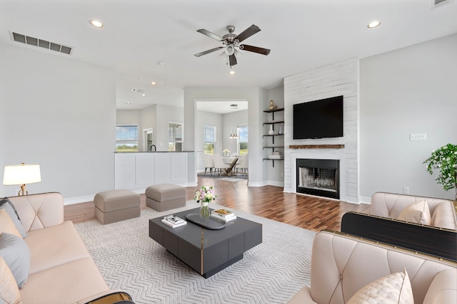 living room featuring ceiling fan, a large fireplace, sink, and light wood-type flooring