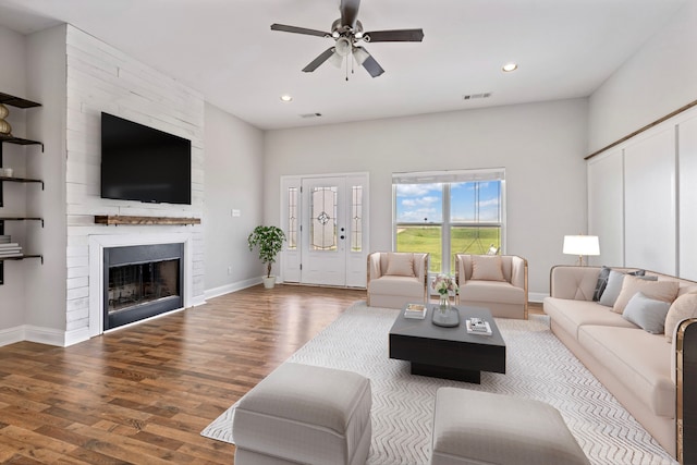 living room featuring hardwood / wood-style floors, a large fireplace, and ceiling fan