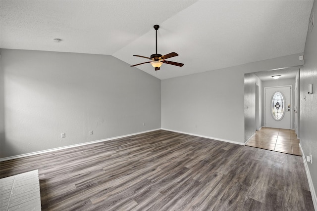 unfurnished living room featuring vaulted ceiling, dark wood-type flooring, a textured ceiling, and ceiling fan